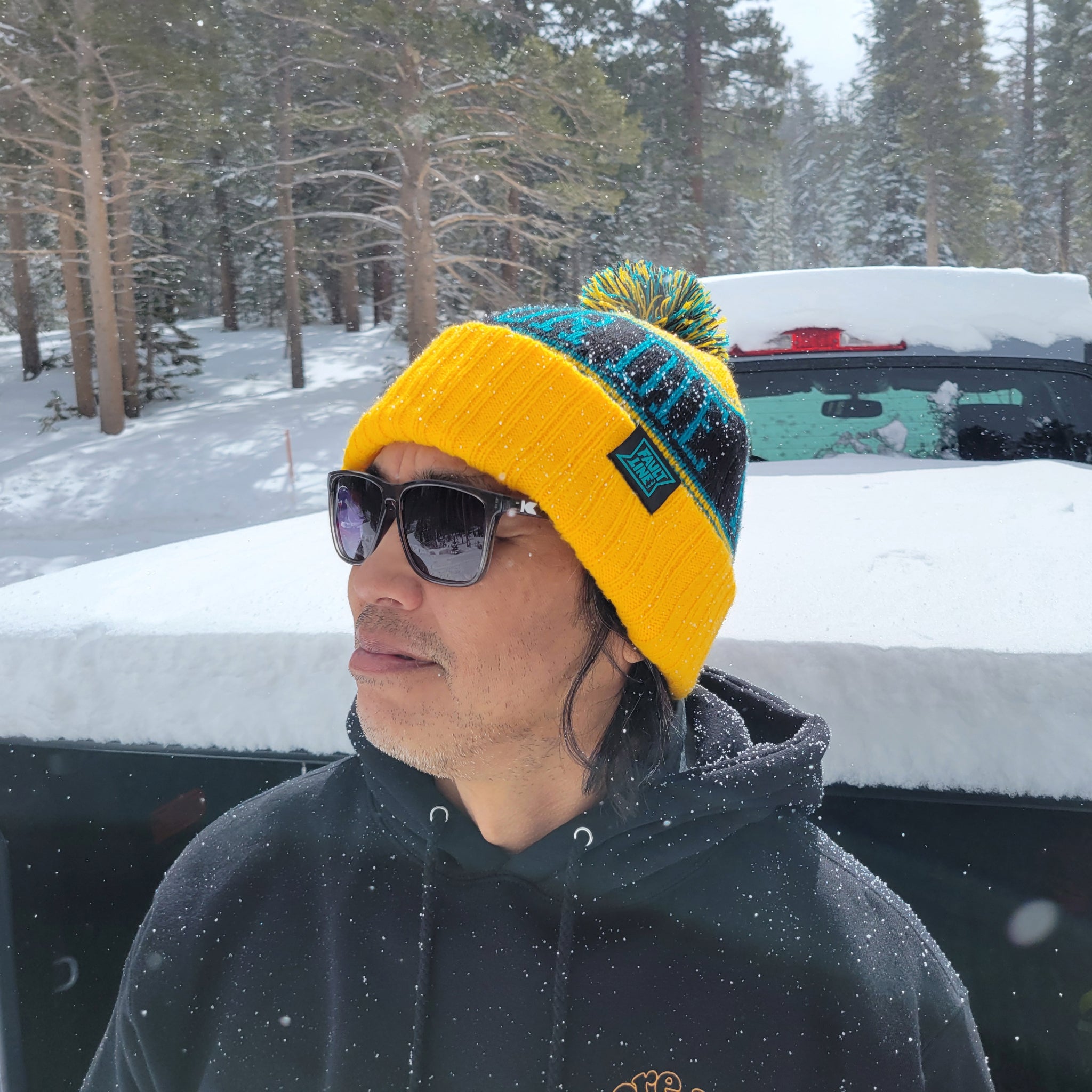 Model wearing a Ride or Die Beanie while it's snowing in the mountains.